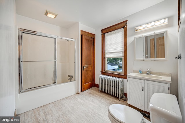 full bathroom featuring radiator, vanity, toilet, bath / shower combo with glass door, and hardwood / wood-style floors