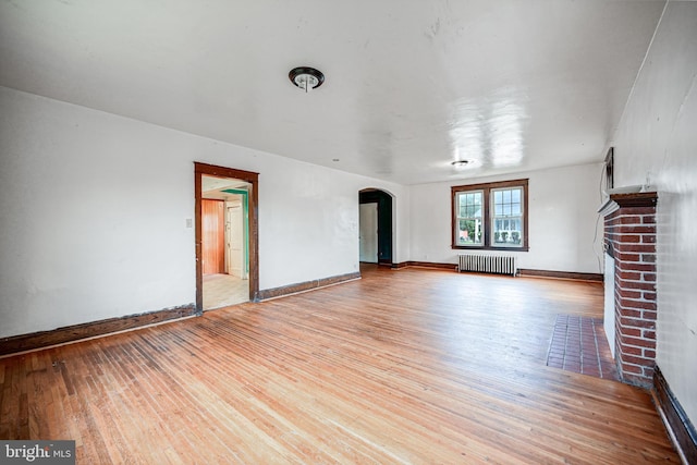 unfurnished living room with radiator heating unit, light wood-type flooring, and a fireplace