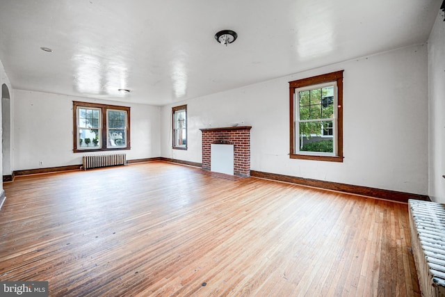 unfurnished living room featuring a fireplace, radiator heating unit, and hardwood / wood-style flooring