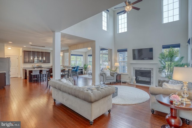 living room with ceiling fan, dark hardwood / wood-style flooring, a high end fireplace, and a high ceiling