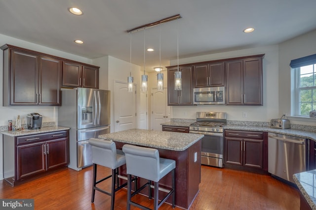 kitchen featuring appliances with stainless steel finishes, light stone countertops, dark hardwood / wood-style flooring, a center island, and decorative light fixtures