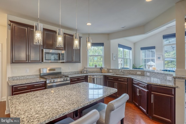 kitchen with a breakfast bar, light stone countertops, dark hardwood / wood-style flooring, stainless steel appliances, and decorative light fixtures