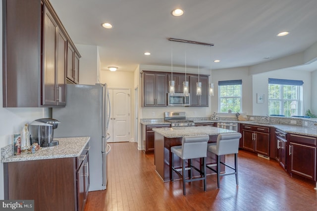 kitchen with a center island, hanging light fixtures, stainless steel appliances, dark hardwood / wood-style flooring, and light stone countertops