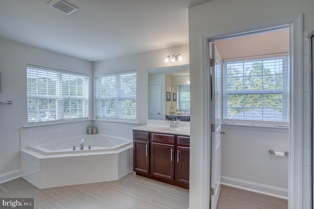 bathroom featuring a relaxing tiled tub, vanity, and tile patterned floors