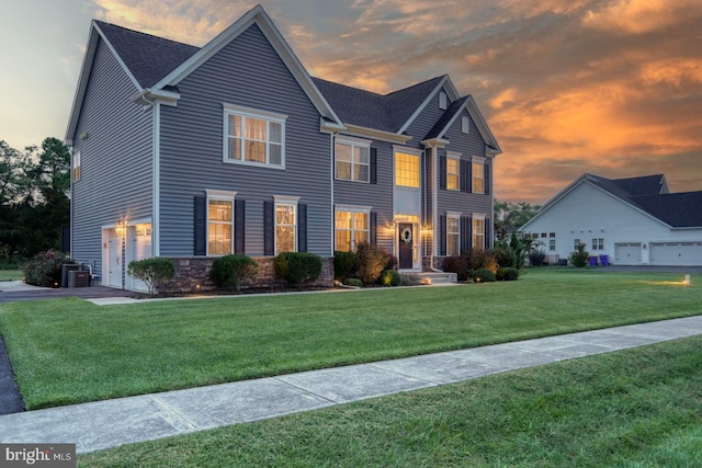 colonial-style house featuring a garage, a lawn, and central AC