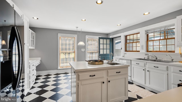 kitchen featuring black refrigerator with ice dispenser, a kitchen island, white cabinetry, pendant lighting, and sink