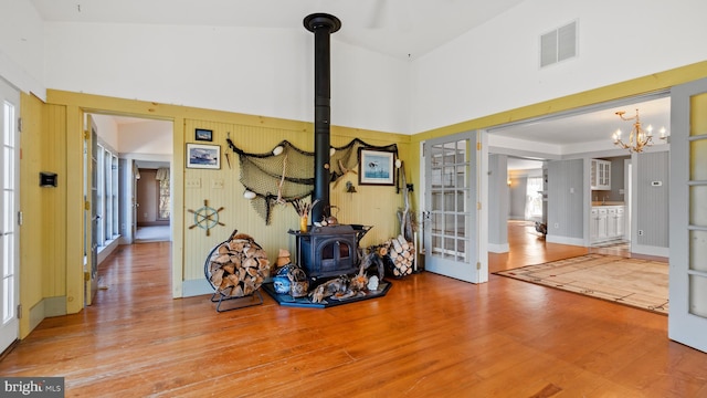 miscellaneous room with high vaulted ceiling, a chandelier, wood-type flooring, and a wood stove