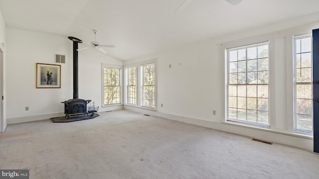 unfurnished living room with vaulted ceiling, light colored carpet, a wood stove, and ceiling fan