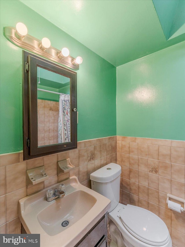 bathroom with walk in shower, vanity, toilet, and tile walls