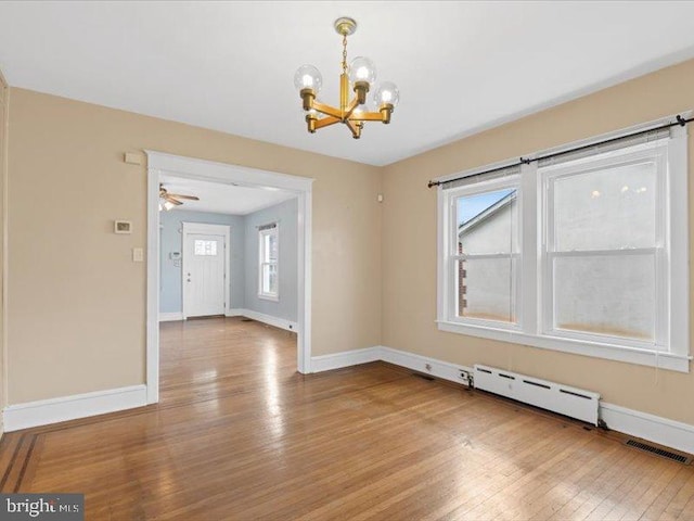 empty room featuring wood-type flooring, baseboard heating, and a healthy amount of sunlight