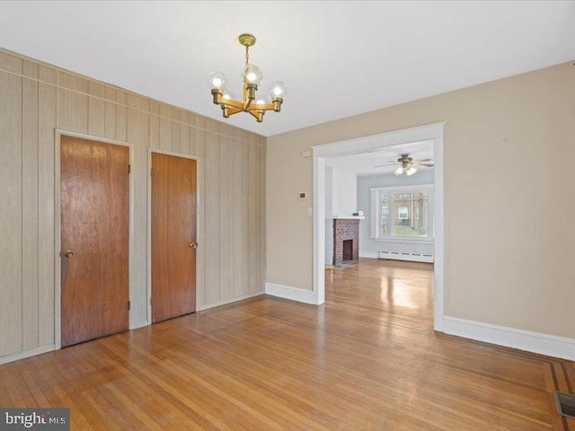 unfurnished dining area featuring ceiling fan with notable chandelier, a baseboard radiator, a fireplace, and light wood-type flooring