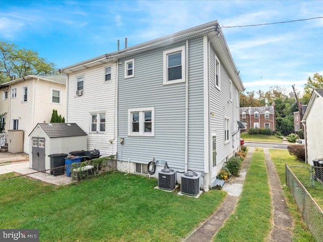 rear view of house featuring cooling unit, a storage shed, and a lawn