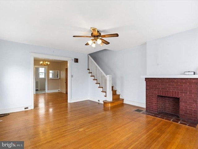 unfurnished living room featuring ceiling fan with notable chandelier, hardwood / wood-style floors, and a brick fireplace