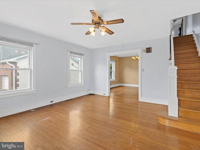 empty room with ceiling fan with notable chandelier and light hardwood / wood-style floors