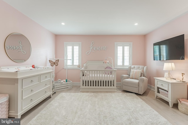 bedroom with light hardwood / wood-style flooring and a nursery area