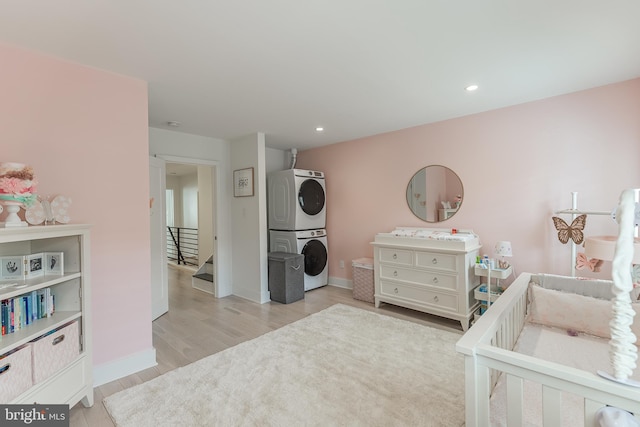 bedroom with light hardwood / wood-style flooring, stacked washer / dryer, and a nursery area