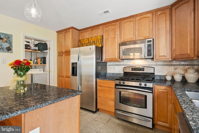 kitchen featuring pendant lighting, decorative backsplash, stainless steel appliances, light tile patterned floors, and washing machine and dryer