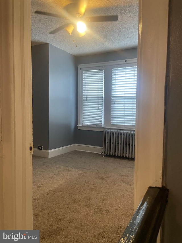 empty room with carpet flooring, ceiling fan, radiator heating unit, and a textured ceiling