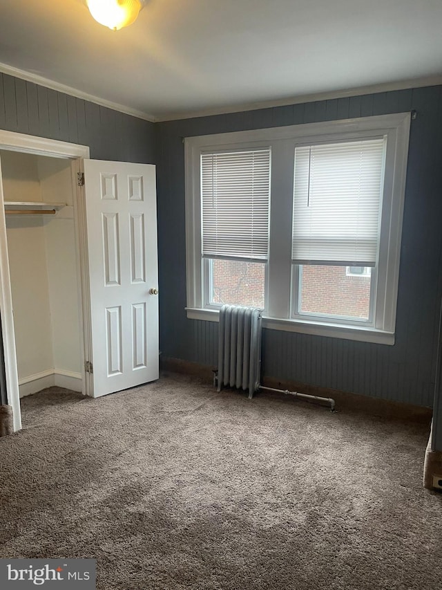 unfurnished bedroom featuring carpet, radiator heating unit, a closet, and crown molding