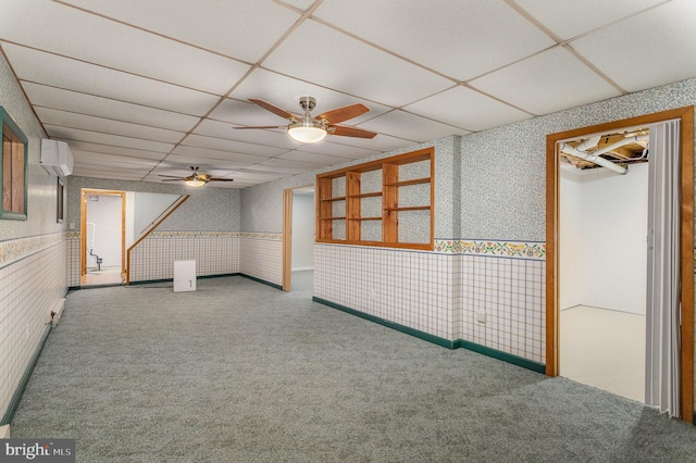 basement featuring a wall mounted air conditioner, a paneled ceiling, carpet floors, and ceiling fan