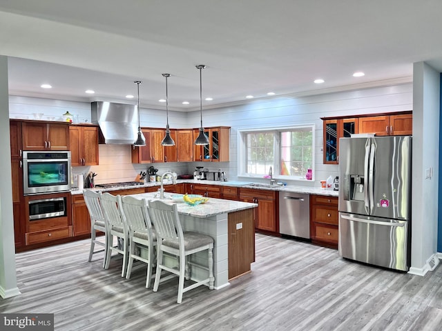 kitchen with wall chimney range hood, a kitchen breakfast bar, stainless steel appliances, a center island with sink, and decorative light fixtures