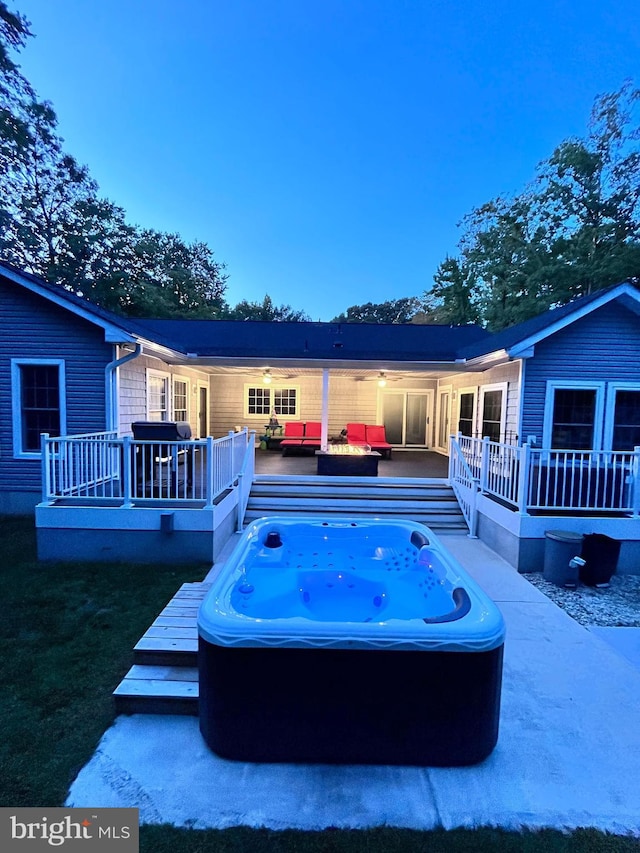 back house at dusk featuring a wooden deck and an outdoor hot tub