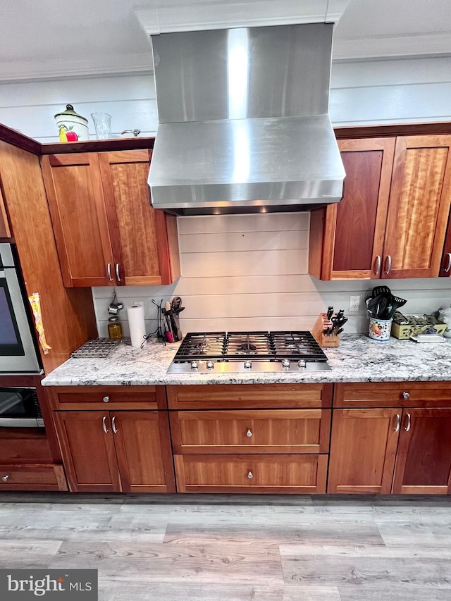 kitchen with light stone countertops, stainless steel appliances, light wood-type flooring, and extractor fan