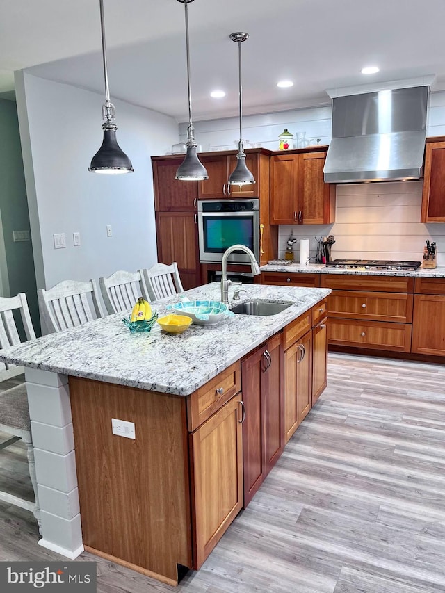 kitchen featuring a kitchen island with sink, light wood-type flooring, a kitchen bar, and wall chimney range hood