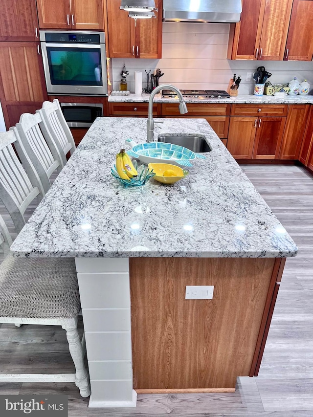 kitchen featuring a kitchen island with sink, light hardwood / wood-style flooring, sink, and extractor fan