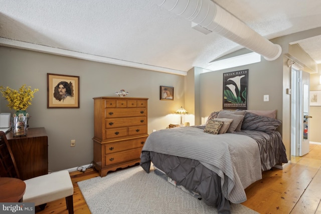 bedroom with a textured ceiling, light hardwood / wood-style floors, and lofted ceiling