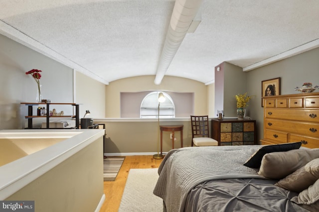 bedroom with light wood-type flooring, vaulted ceiling with beams, and a textured ceiling