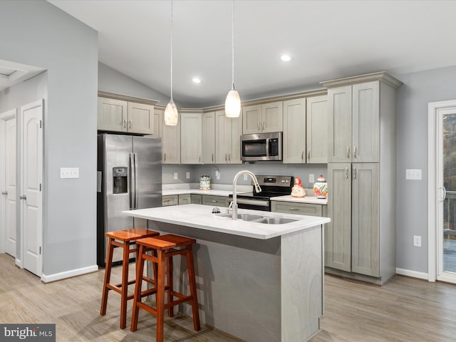 kitchen with appliances with stainless steel finishes, a kitchen island with sink, vaulted ceiling, light hardwood / wood-style flooring, and decorative light fixtures