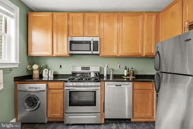 kitchen with dark tile patterned flooring, washer / clothes dryer, appliances with stainless steel finishes, and dark stone counters