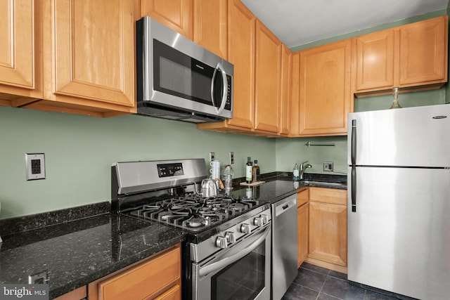 kitchen featuring dark tile patterned flooring, appliances with stainless steel finishes, sink, and dark stone countertops