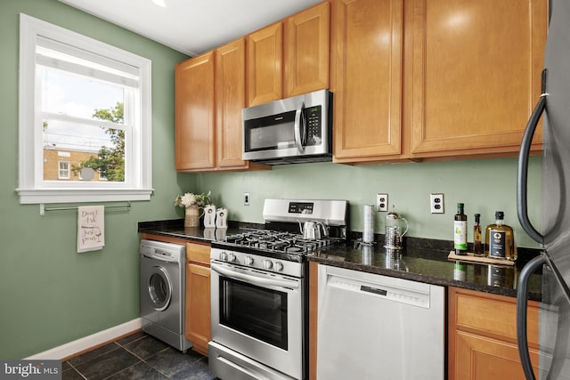 kitchen with dark stone counters, washer / clothes dryer, dark tile patterned floors, and stainless steel appliances