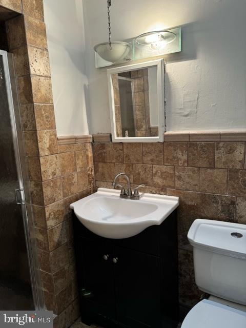 bathroom with tile walls, vanity, toilet, and a shower with door