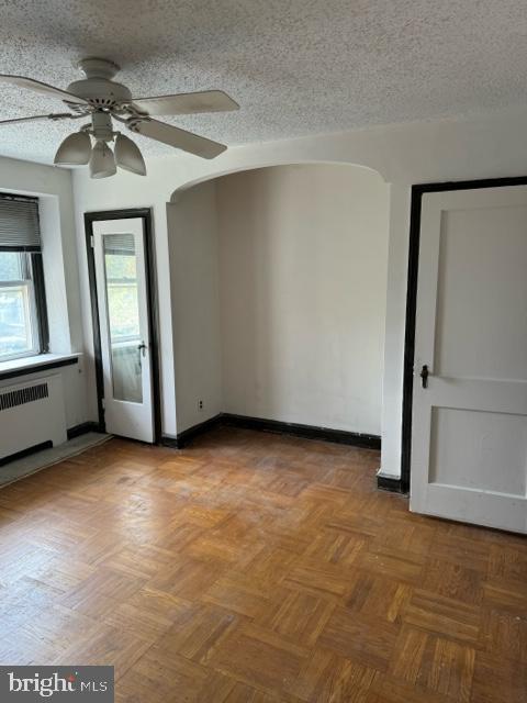 unfurnished room featuring radiator heating unit, ceiling fan, light parquet floors, and a textured ceiling