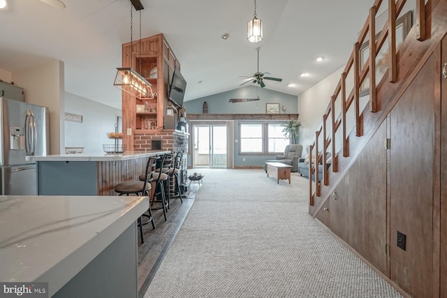 interior space featuring a breakfast bar, stainless steel refrigerator with ice dispenser, light carpet, decorative light fixtures, and ceiling fan