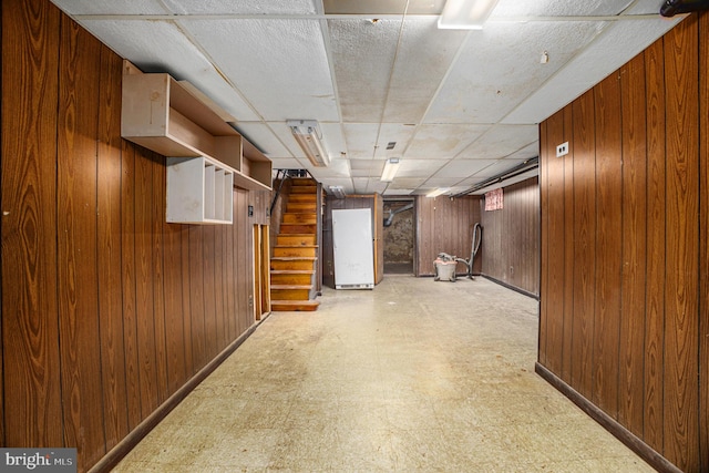 basement with a paneled ceiling and wood walls