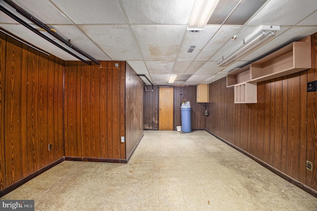 basement with a drop ceiling, wood walls, and light colored carpet