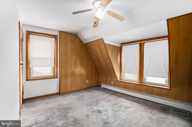 additional living space with wood walls, lofted ceiling, ceiling fan, a baseboard radiator, and light colored carpet