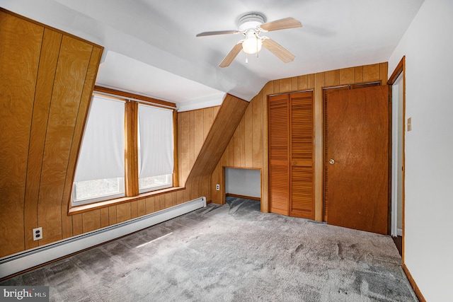 bonus room featuring ceiling fan, dark colored carpet, wooden walls, and a baseboard heating unit