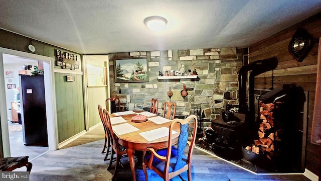 dining room featuring a textured ceiling, wood walls, a wood stove, and hardwood / wood-style flooring