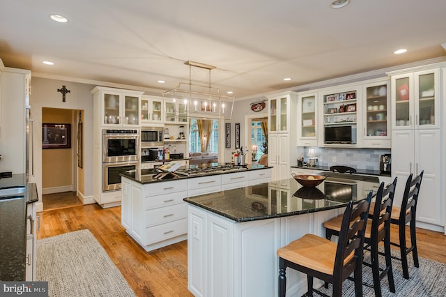 kitchen featuring appliances with stainless steel finishes, a center island, decorative light fixtures, white cabinets, and crown molding