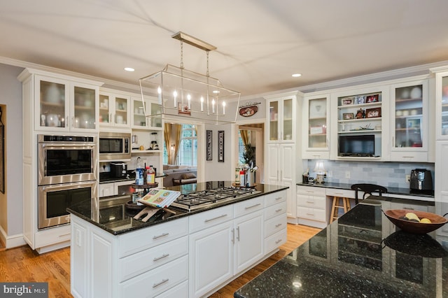 kitchen featuring white cabinets, appliances with stainless steel finishes, dark stone countertops, pendant lighting, and crown molding