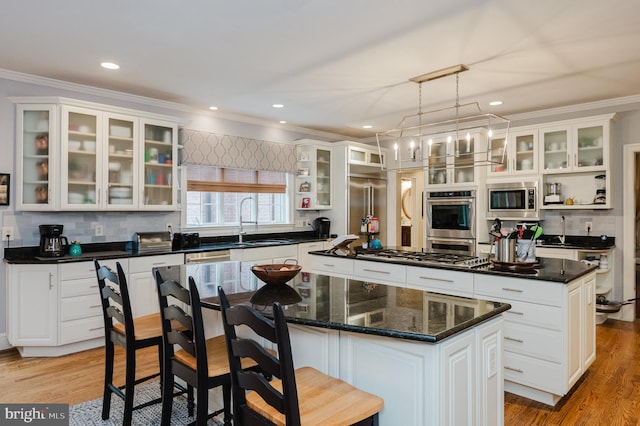 kitchen with white cabinets, hanging light fixtures, a kitchen island, light wood-type flooring, and built in appliances