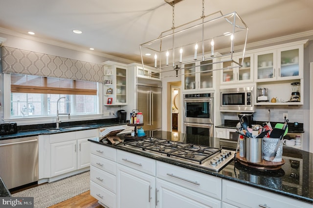 kitchen with built in appliances, hanging light fixtures, light hardwood / wood-style flooring, sink, and white cabinets