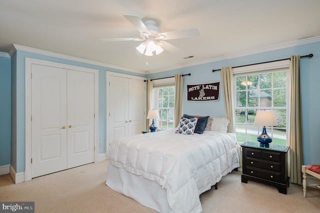 bedroom with light carpet, crown molding, two closets, and ceiling fan