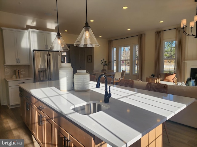 kitchen featuring stainless steel fridge, backsplash, sink, pendant lighting, and an island with sink