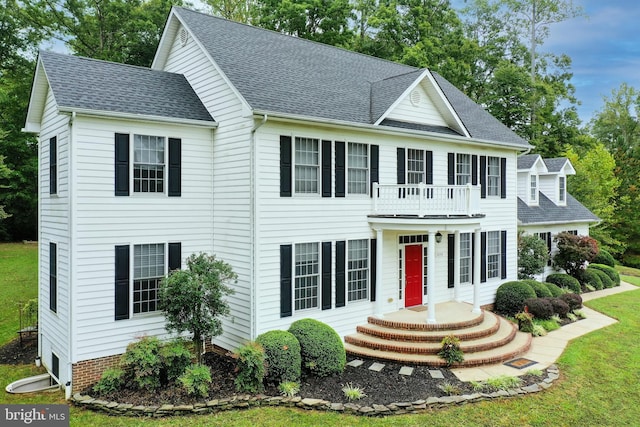 colonial home featuring a balcony and a front lawn